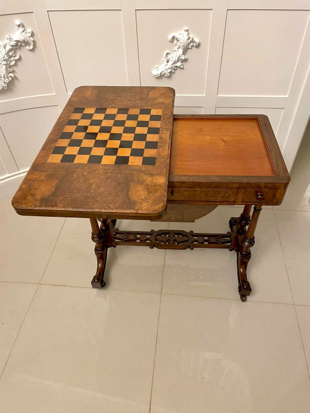 An antique Victorian burr walnut games table featuring an inlaid chessboard top, a frieze drawer, carved turned twin-column supports, and a pierced fretwork stretcher. View IV
