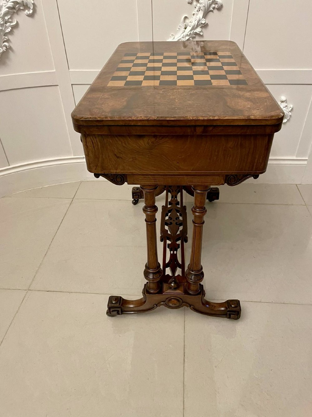 An antique Victorian burr walnut games table featuring an inlaid chessboard top, a frieze drawer, carved turned twin-column supports, and a pierced fretwork stretcher. View VII