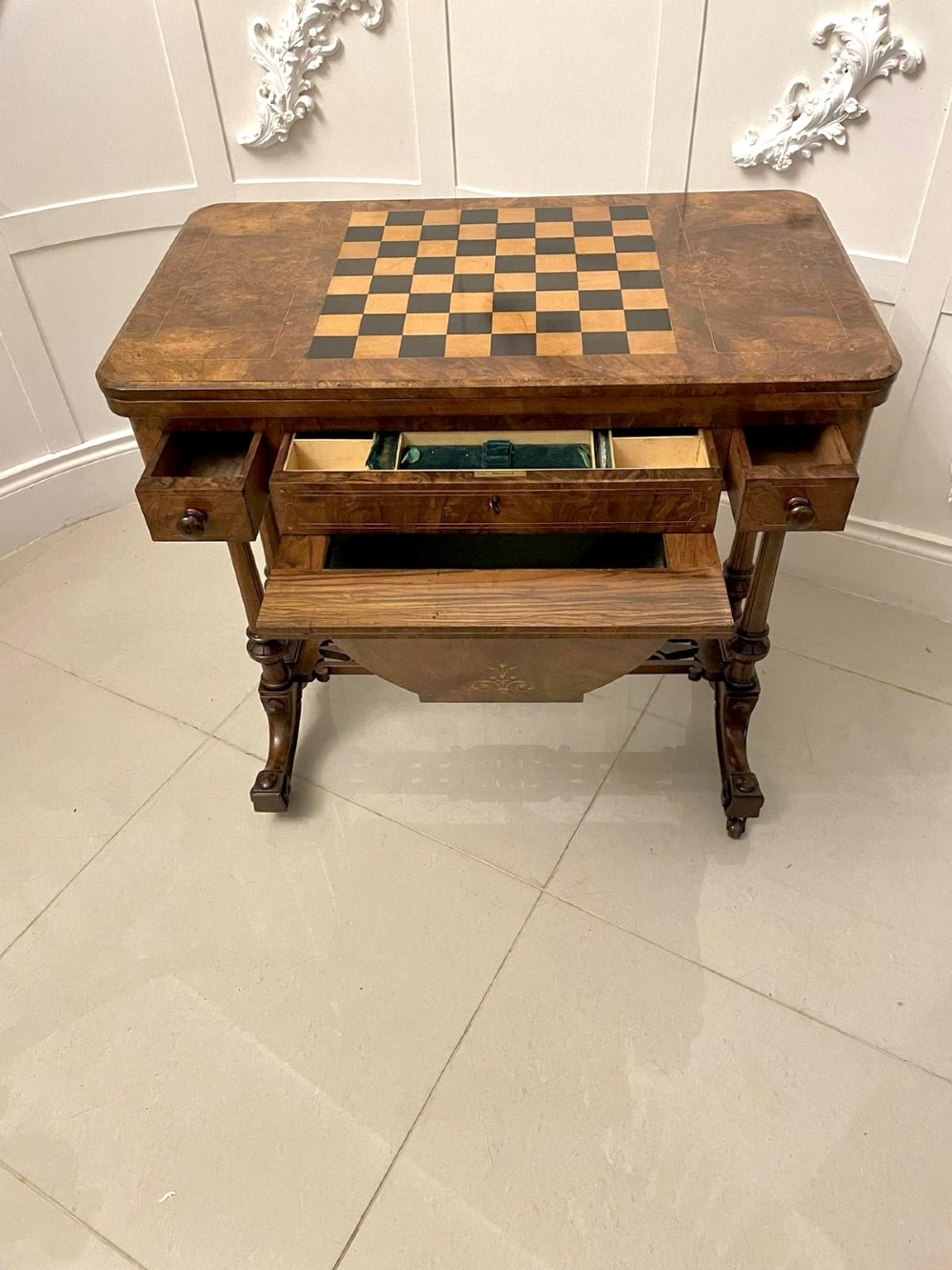 An antique Victorian burr walnut games table featuring an inlaid chessboard top, a frieze drawer, carved turned twin-column supports, and a pierced fretwork stretcher. View IX
