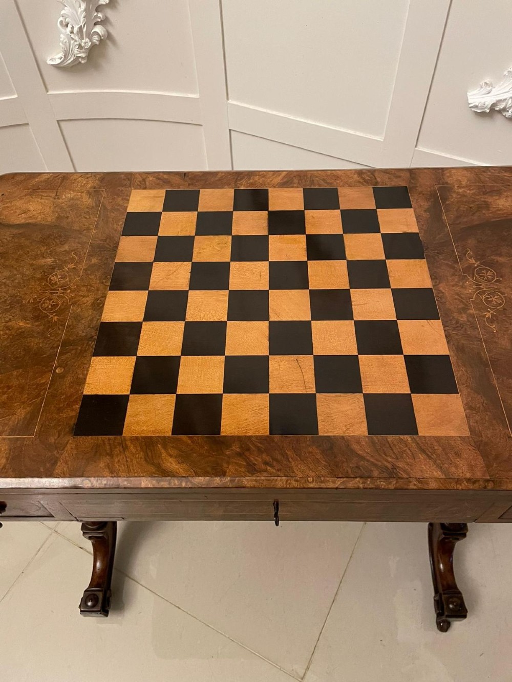 An antique Victorian burr walnut games table featuring an inlaid chessboard top, a frieze drawer, carved turned twin-column supports, and a pierced fretwork stretcher. View XIII