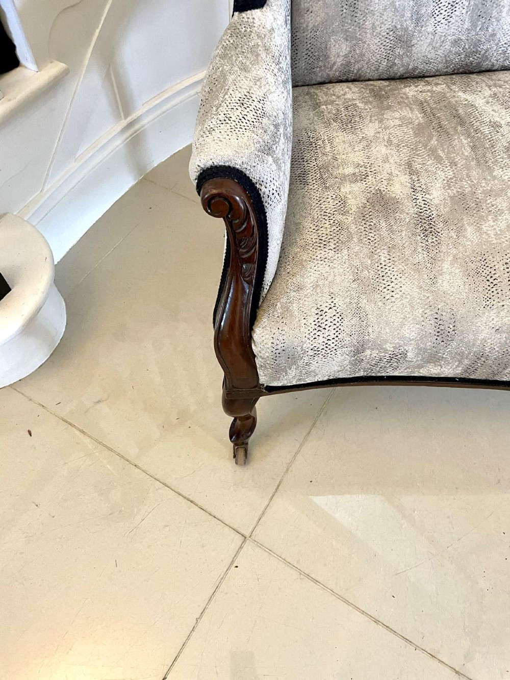 Victorian carved mahogany sofa featuring a decorative crest rail, curved scroll arms, grey textured upholstery, and cabriole legs on brass castors. View VI