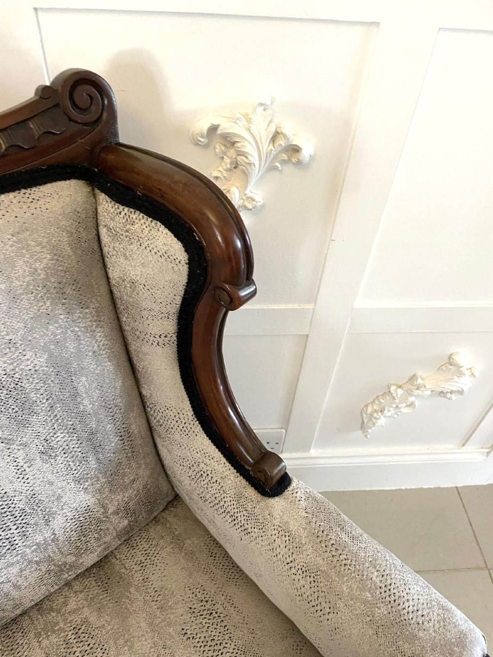 Victorian carved mahogany sofa featuring a decorative crest rail, curved scroll arms, grey textured upholstery, and cabriole legs on brass castors. View VII