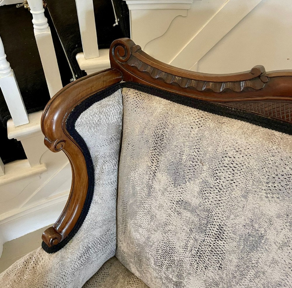 Victorian carved mahogany sofa featuring a decorative crest rail, curved scroll arms, grey textured upholstery, and cabriole legs on brass castors. View IX
