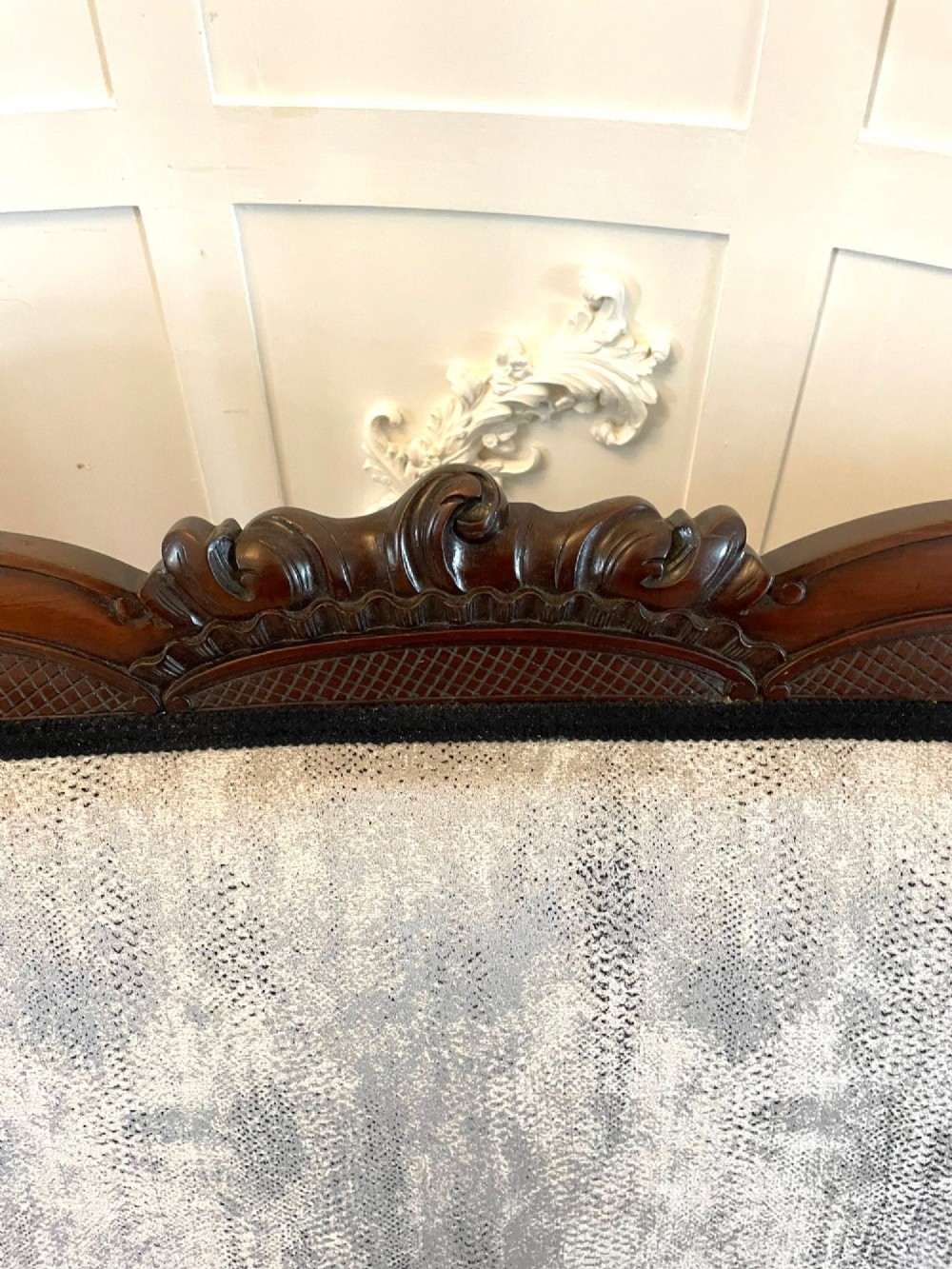 Victorian carved mahogany sofa featuring a decorative crest rail, curved scroll arms, grey textured upholstery, and cabriole legs on brass castors. View X