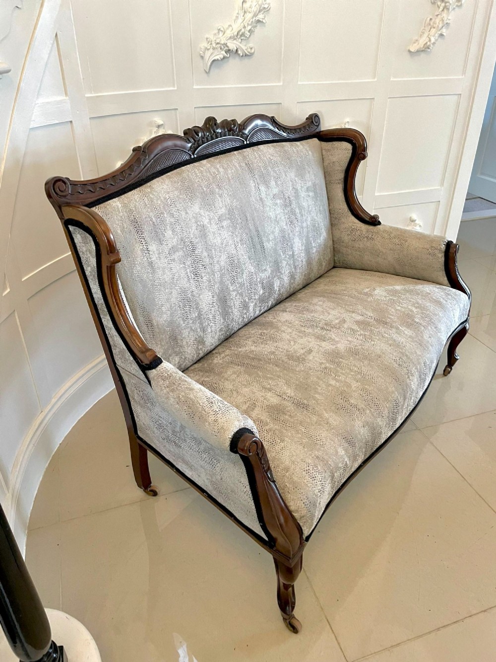 Victorian carved mahogany sofa featuring a decorative crest rail, curved scroll arms, grey textured upholstery, and cabriole legs on brass castors. View XI