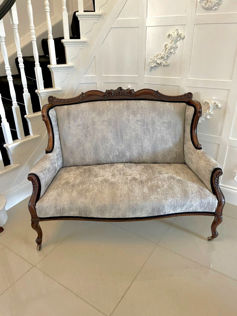 Victorian carved mahogany sofa featuring a decorative crest rail, curved scroll arms, grey textured upholstery, and cabriole legs on brass castors. View XII