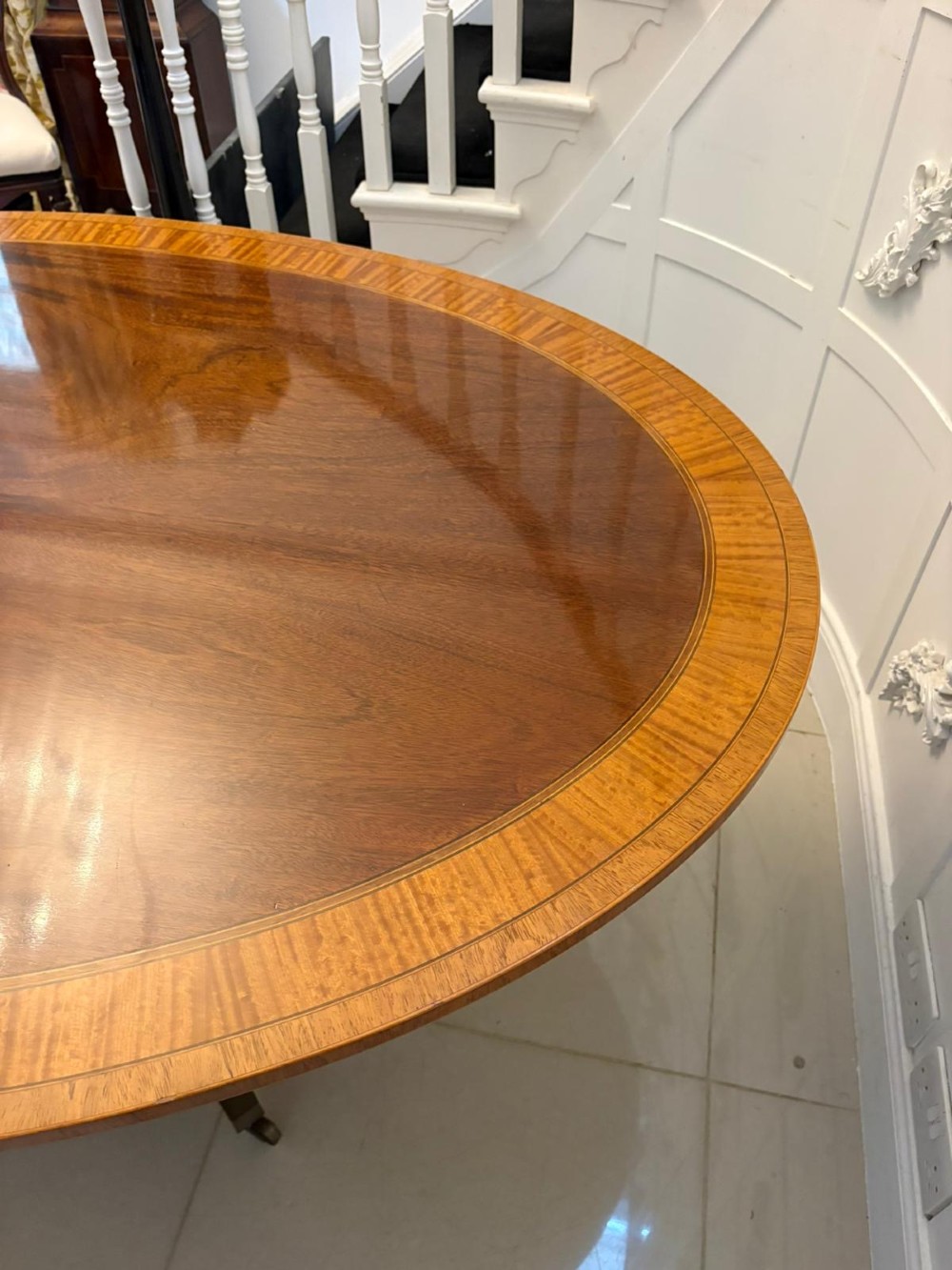 An antique Regency style oval mahogany tilt-top dining table featuring a figured timber top with satinwood crossbanding mounted on a pedestal base with brass castors. View VI