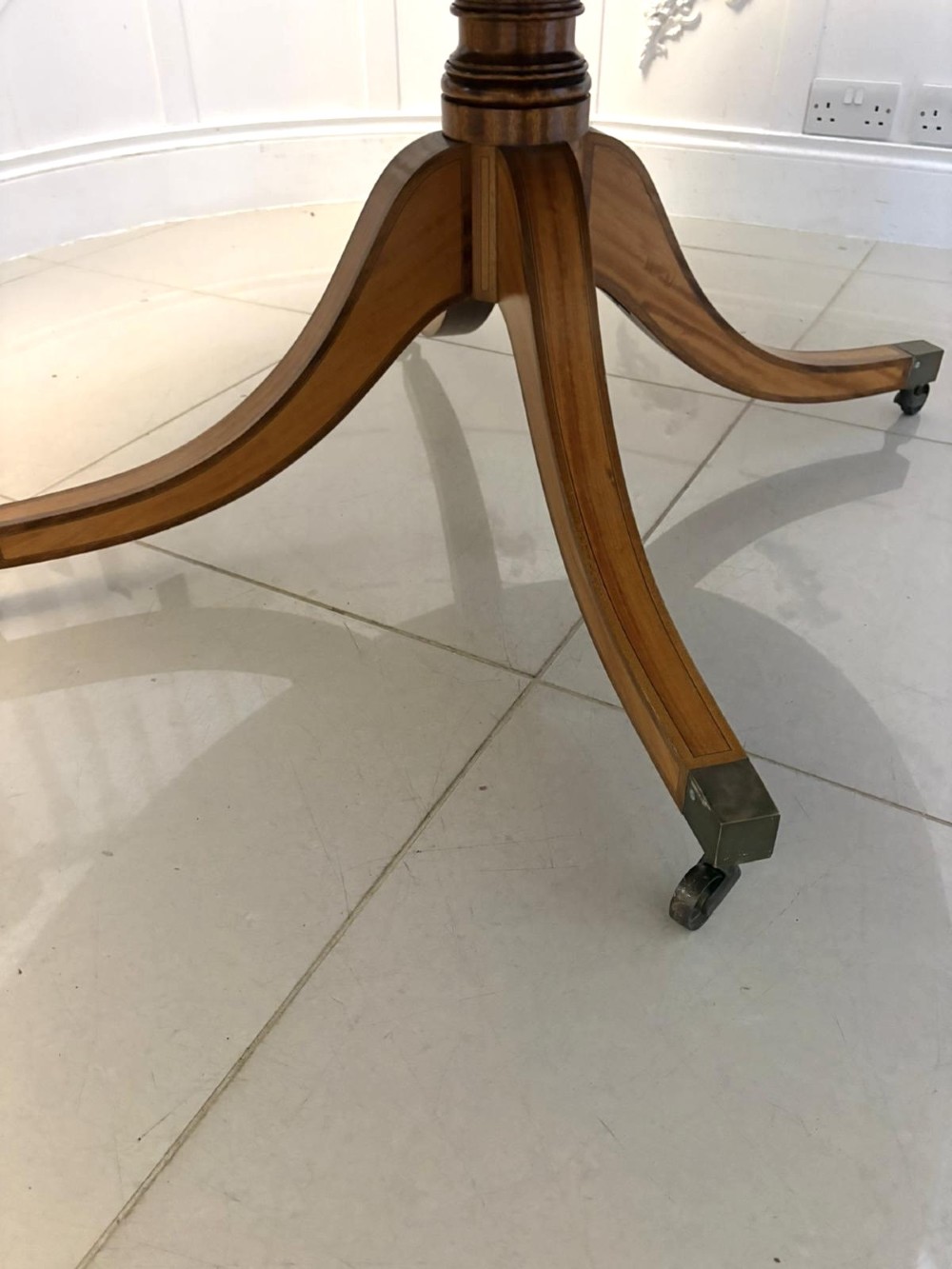 An antique Regency style oval mahogany tilt-top dining table featuring a figured timber top with satinwood crossbanding mounted on a pedestal base with brass castors. View XI