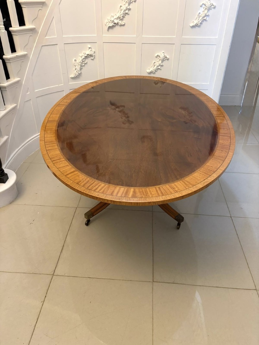 An antique Regency style oval mahogany tilt-top dining table featuring a figured timber top with satinwood crossbanding mounted on a pedestal base with brass castors. View XII