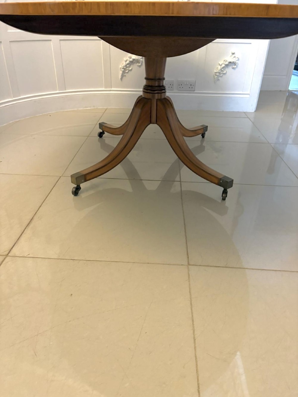 An antique Regency style oval mahogany tilt-top dining table featuring a figured timber top with satinwood crossbanding mounted on a pedestal base with brass castors. View XIII