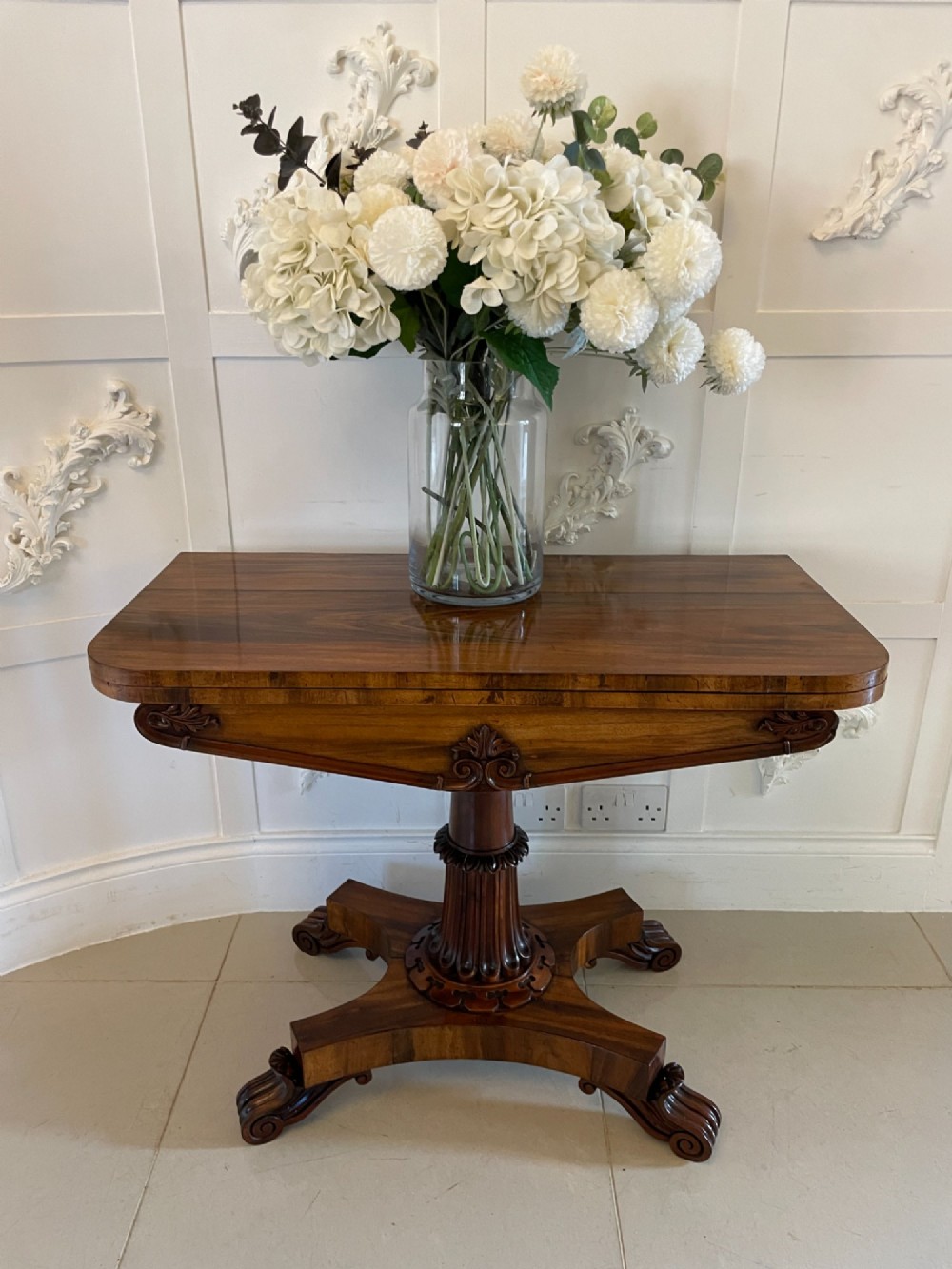 An antique Victorian rosewood fold-over card table featuring a carved frieze, a fluted pedestal column, and a quadform base with scroll feet. View II