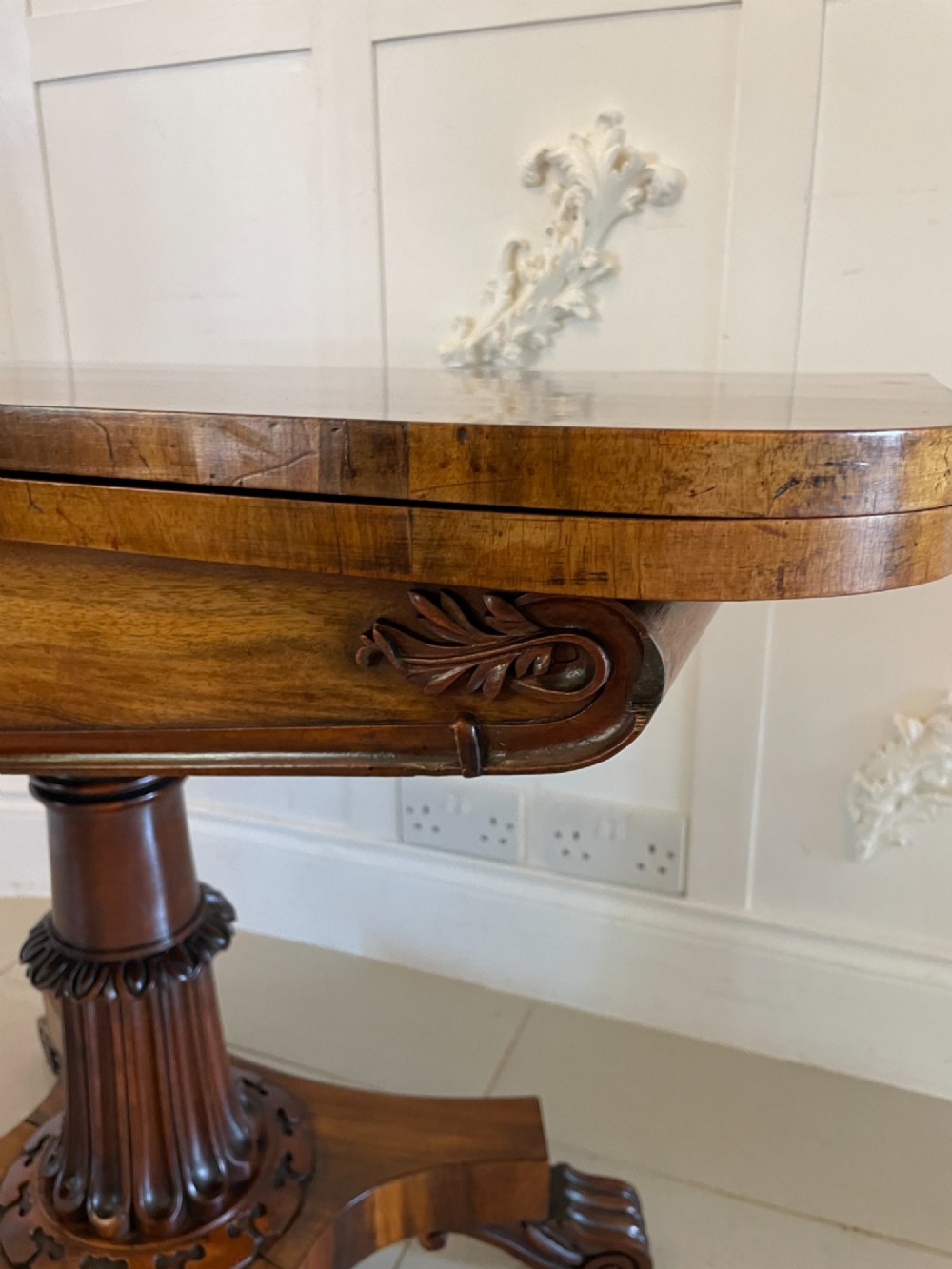 An antique Victorian rosewood fold-over card table featuring a carved frieze, a fluted pedestal column, and a quadform base with scroll feet. View XI