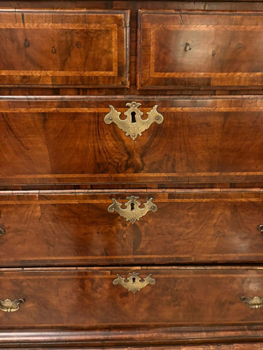 An early eighteenth-century George I walnut chest on stand featuring crossbanded drawers, brass drop handles, and cabriole legs with pad feet. View V
