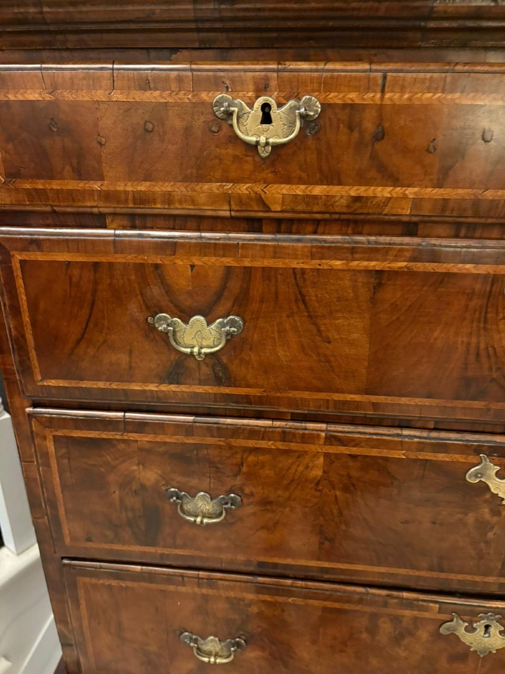 An early eighteenth-century George I walnut chest on stand featuring crossbanded drawers, brass drop handles, and cabriole legs with pad feet. View VI