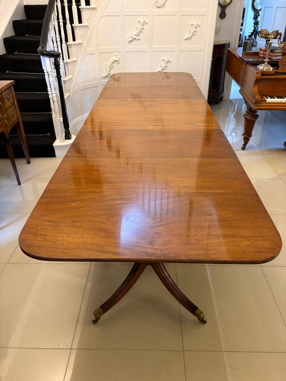 A long polished mahogany extending dining table supported by three pedestal bases with brass castors.