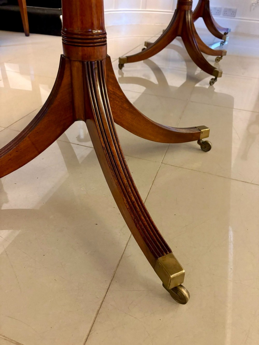 A long polished mahogany extending dining table supported by three pedestal bases with brass castors. View IX