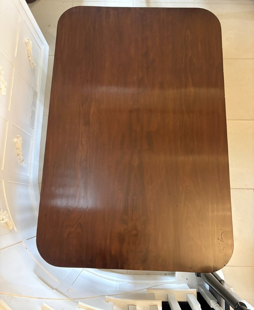 A William IV figured mahogany tilt top dining table shown upright, featuring rounded corners, a smooth grain finish, and a central pedestal base with carved feet. View IV