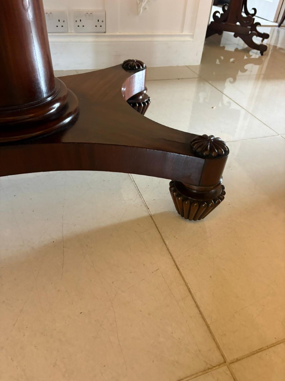 A William IV figured mahogany tilt top dining table shown upright, featuring rounded corners, a smooth grain finish, and a central pedestal base with carved feet. View V