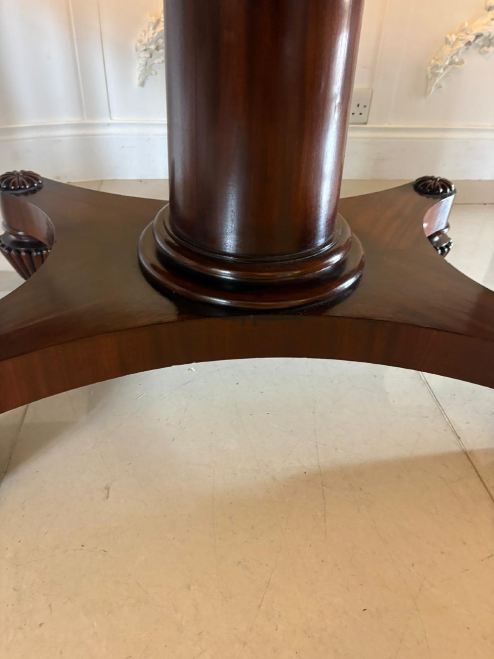 A William IV figured mahogany tilt top dining table shown upright, featuring rounded corners, a smooth grain finish, and a central pedestal base with carved feet. View VI