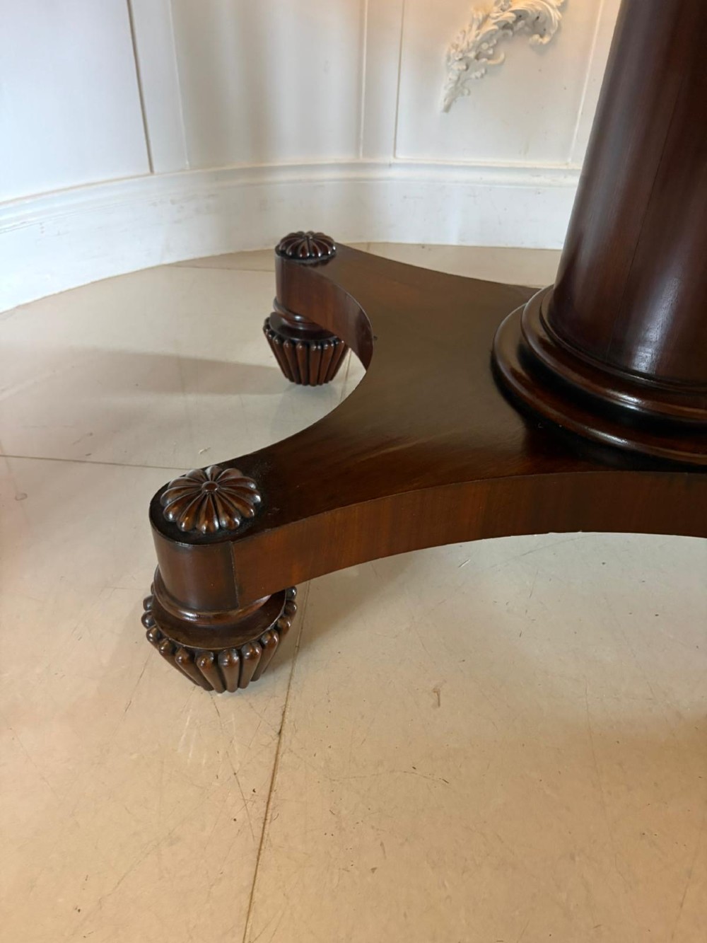 A William IV figured mahogany tilt top dining table shown upright, featuring rounded corners, a smooth grain finish, and a central pedestal base with carved feet. View VII