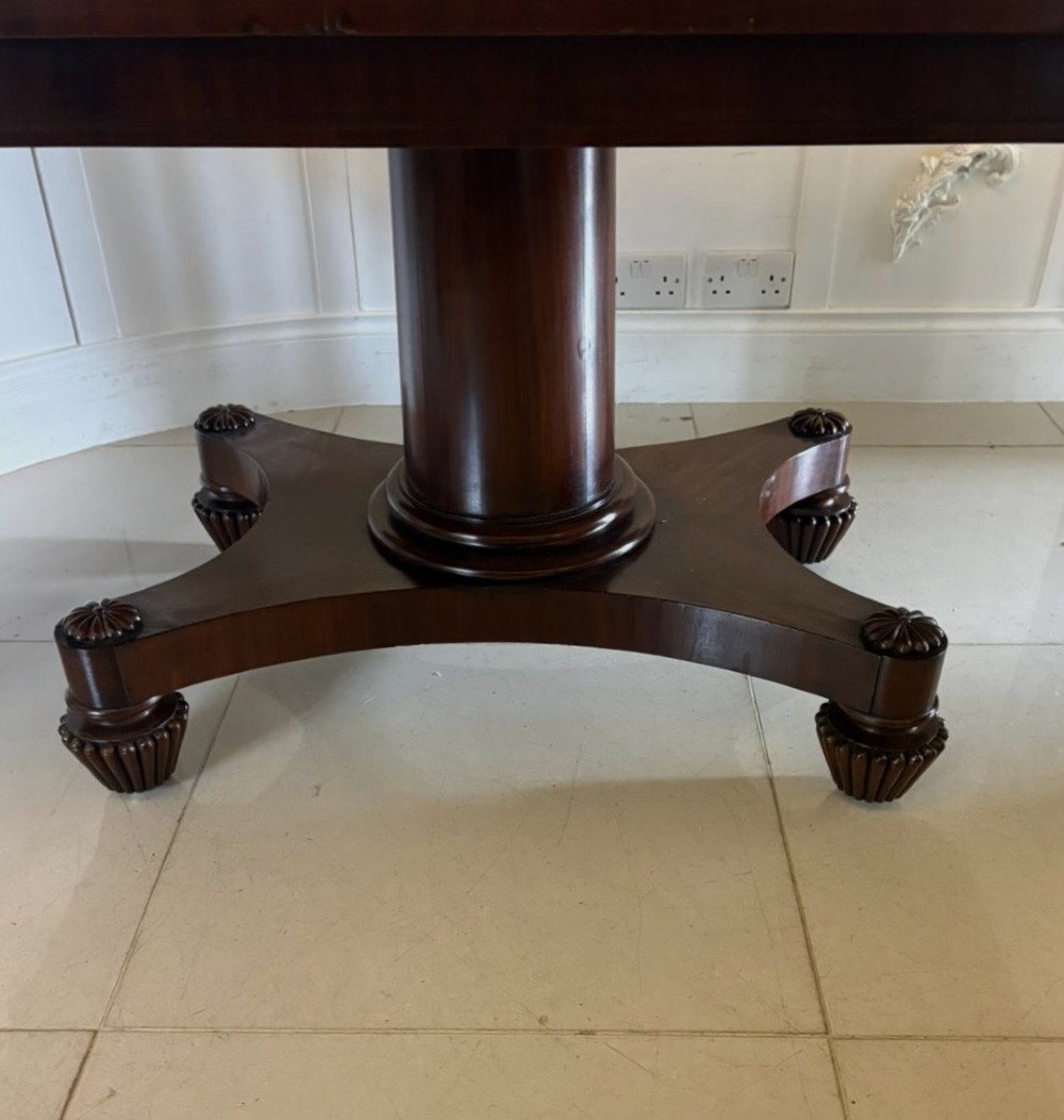 A William IV figured mahogany tilt top dining table shown upright, featuring rounded corners, a smooth grain finish, and a central pedestal base with carved feet. View XI