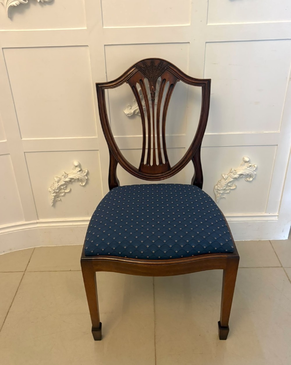 A set of twelve mahogany shield back dining chairs featuring carved backrest splats, square tapered legs, and blue patterned upholstered seats. View II