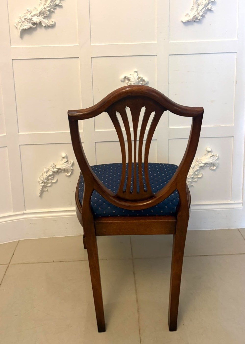 A set of twelve mahogany shield back dining chairs featuring carved backrest splats, square tapered legs, and blue patterned upholstered seats. View IX