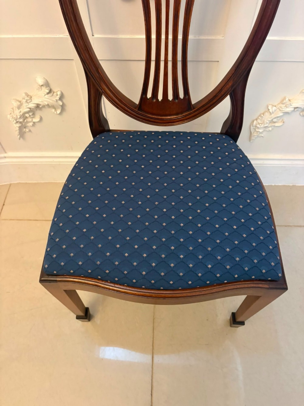 A set of twelve mahogany shield back dining chairs featuring carved backrest splats, square tapered legs, and blue patterned upholstered seats. View X