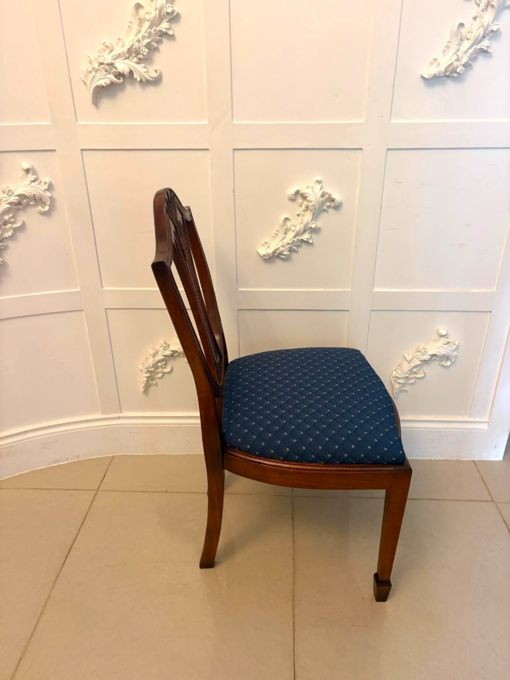 A set of twelve mahogany shield back dining chairs featuring carved backrest splats, square tapered legs, and blue patterned upholstered seats. View XI