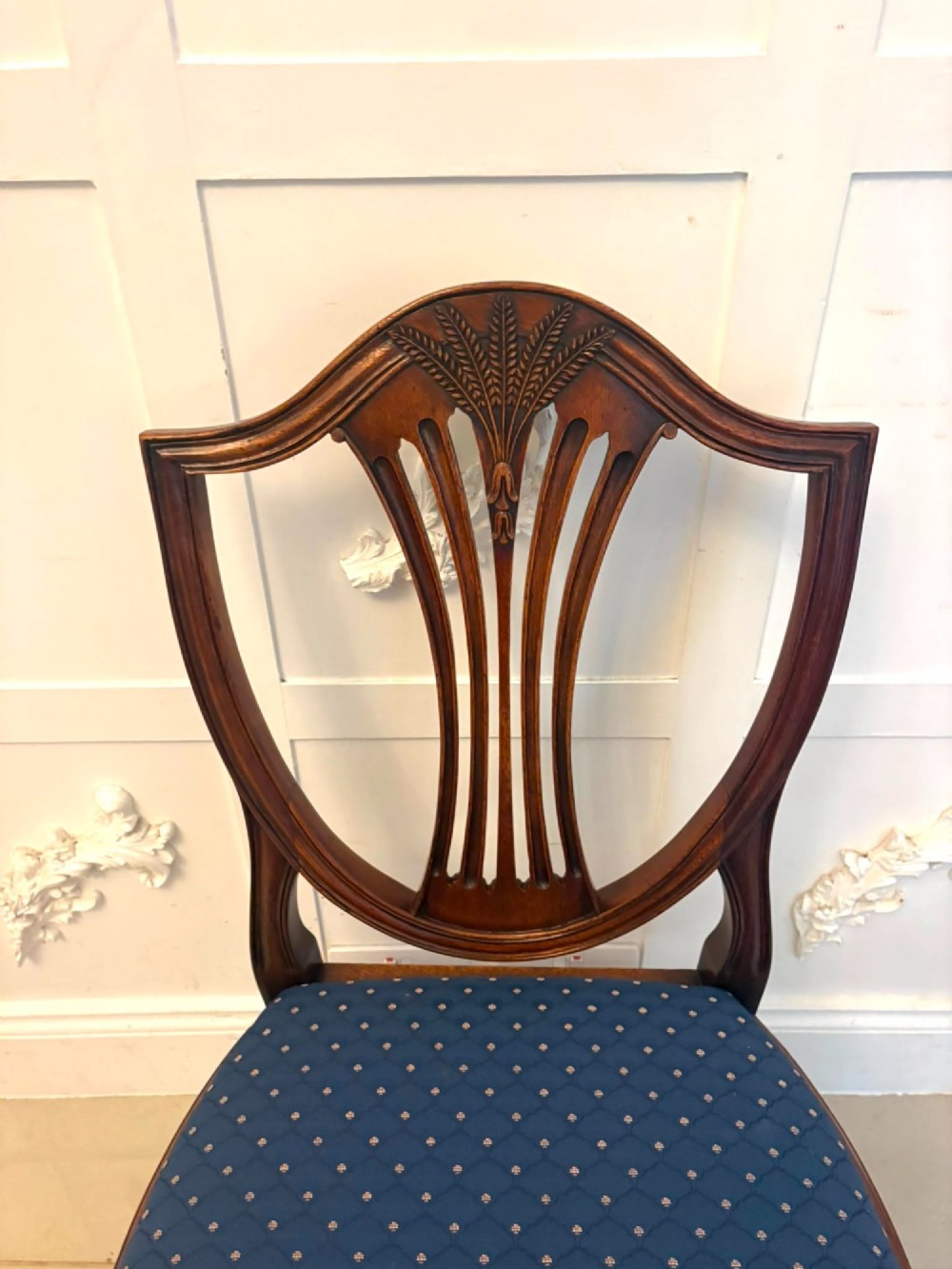 A set of twelve mahogany shield back dining chairs featuring carved backrest splats, square tapered legs, and blue patterned upholstered seats. View XII