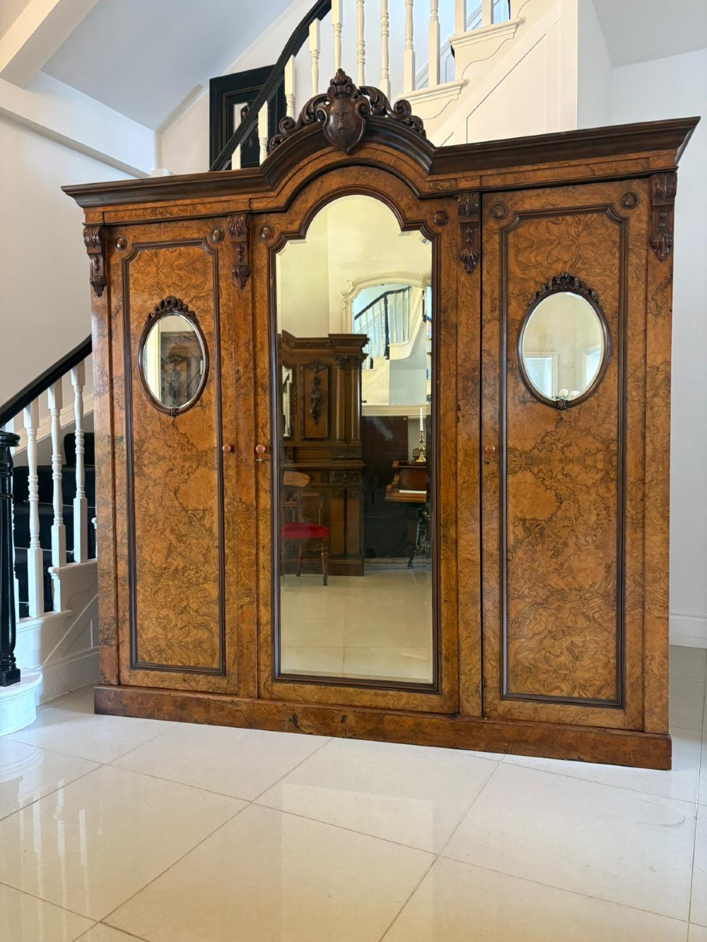 A large Victorian burr walnut three-door wardrobe with a central arched mirrored door, oval mirrors set into side panels, and carved pediment details.