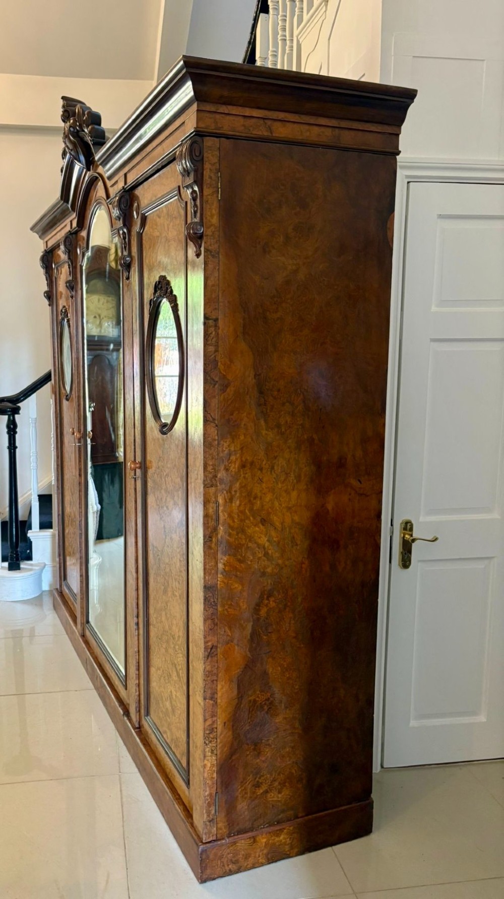 A large Victorian burr walnut three-door wardrobe with a central arched mirrored door, oval mirrors set into side panels, and carved pediment details. View V