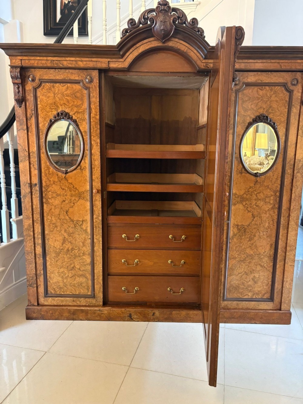 A large Victorian burr walnut three-door wardrobe with a central arched mirrored door, oval mirrors set into side panels, and carved pediment details. View VI