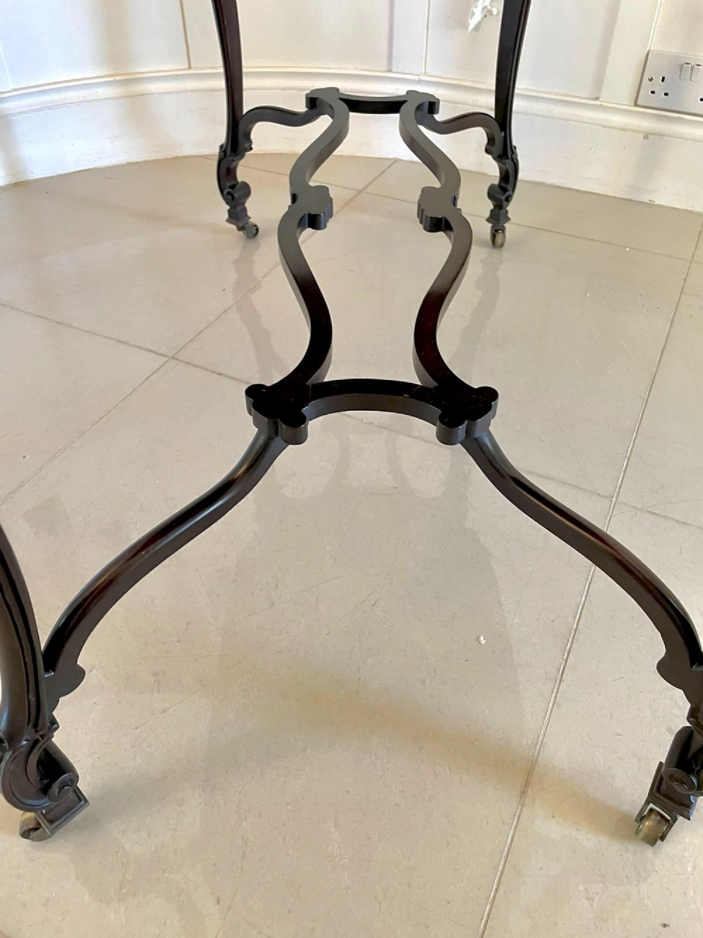 An antique Victorian dark mahogany centre table featuring a shaped serpentine top, carved frieze with brass handles, cabriole legs, and an arched scroll stretcher. View II