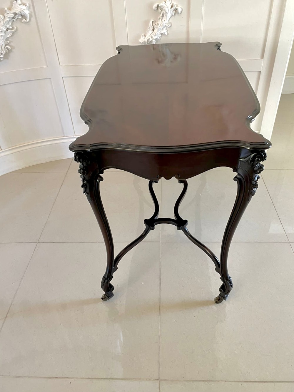 An antique Victorian dark mahogany centre table featuring a shaped serpentine top, carved frieze with brass handles, cabriole legs, and an arched scroll stretcher. View IV