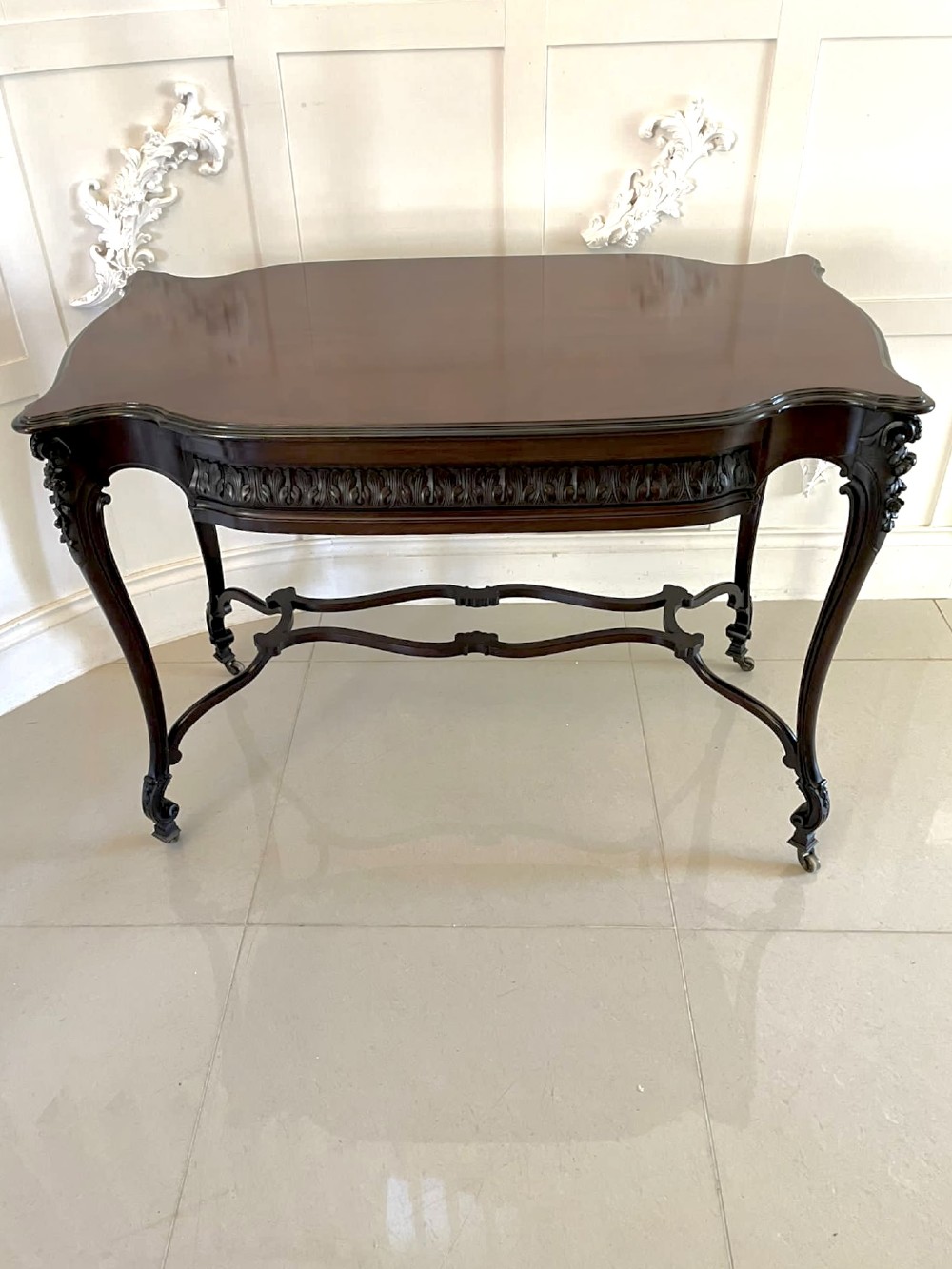An antique Victorian dark mahogany centre table featuring a shaped serpentine top, carved frieze with brass handles, cabriole legs, and an arched scroll stretcher. View V