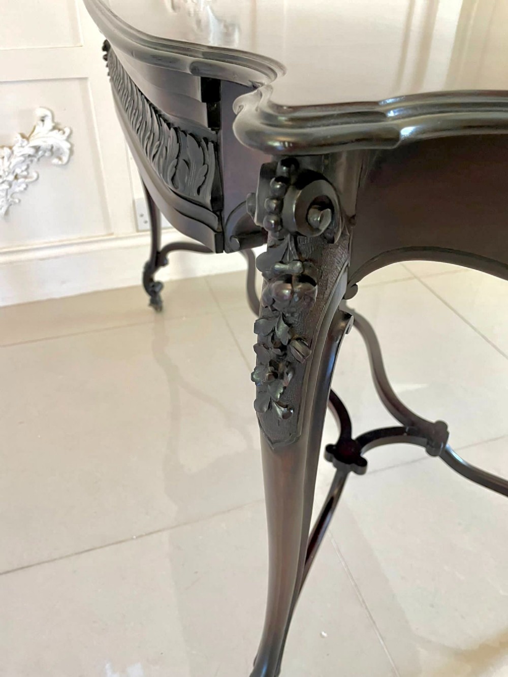 An antique Victorian dark mahogany centre table featuring a shaped serpentine top, carved frieze with brass handles, cabriole legs, and an arched scroll stretcher. View IX