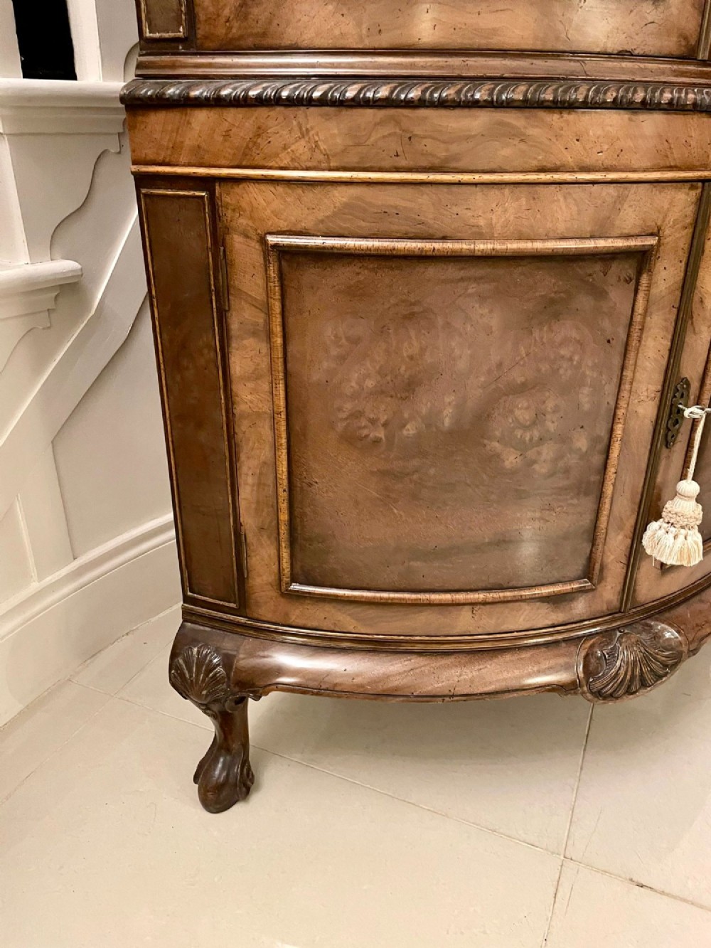 An antique burr walnut bow-fronted cocktail cabinet featuring two upper doors, two lower doors, carved cabriole legs, and brass keyhole escutcheons. View IX