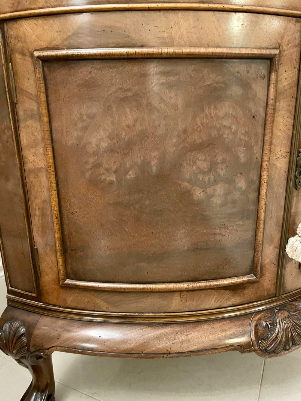 An antique burr walnut bow-fronted cocktail cabinet featuring two upper doors, two lower doors, carved cabriole legs, and brass keyhole escutcheons. View X