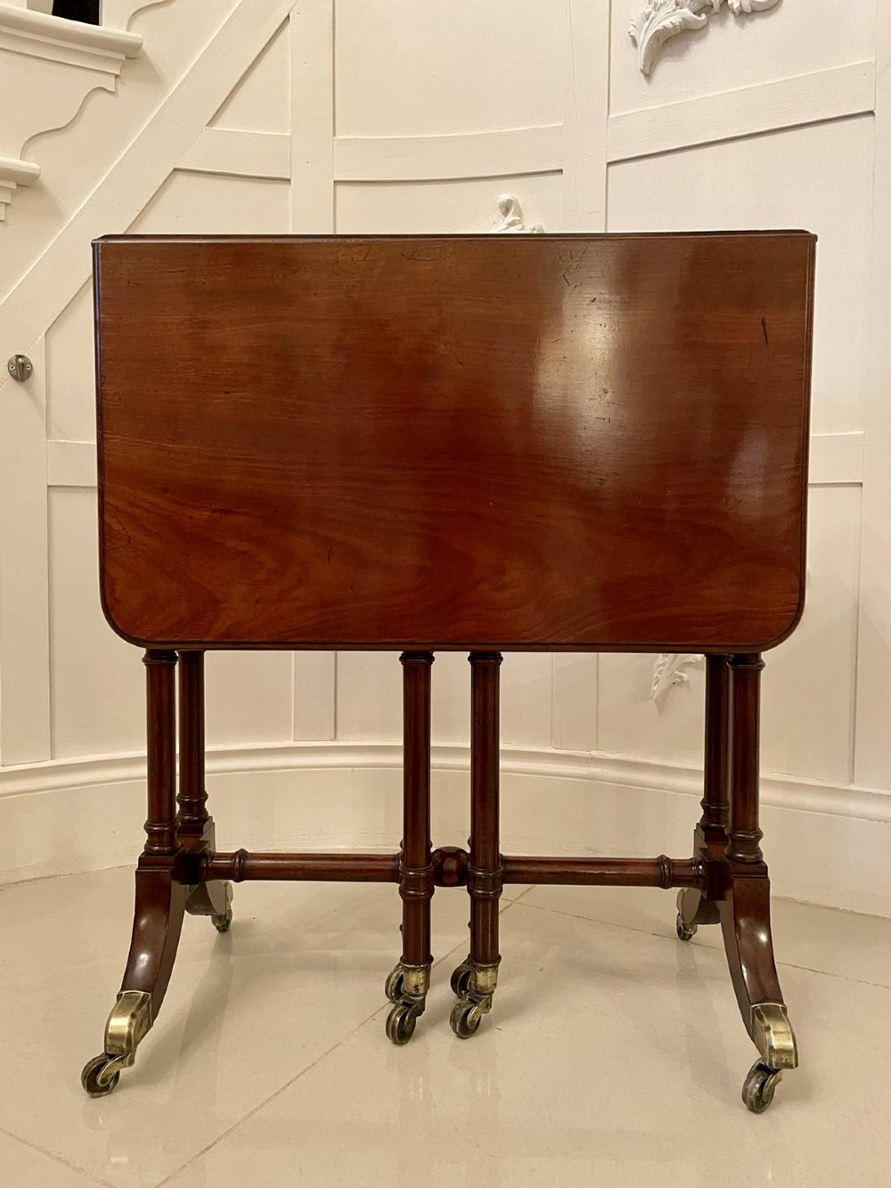 A closed George III mahogany drop-leaf table with slender turned legs, a stretcher base, and brass castors.