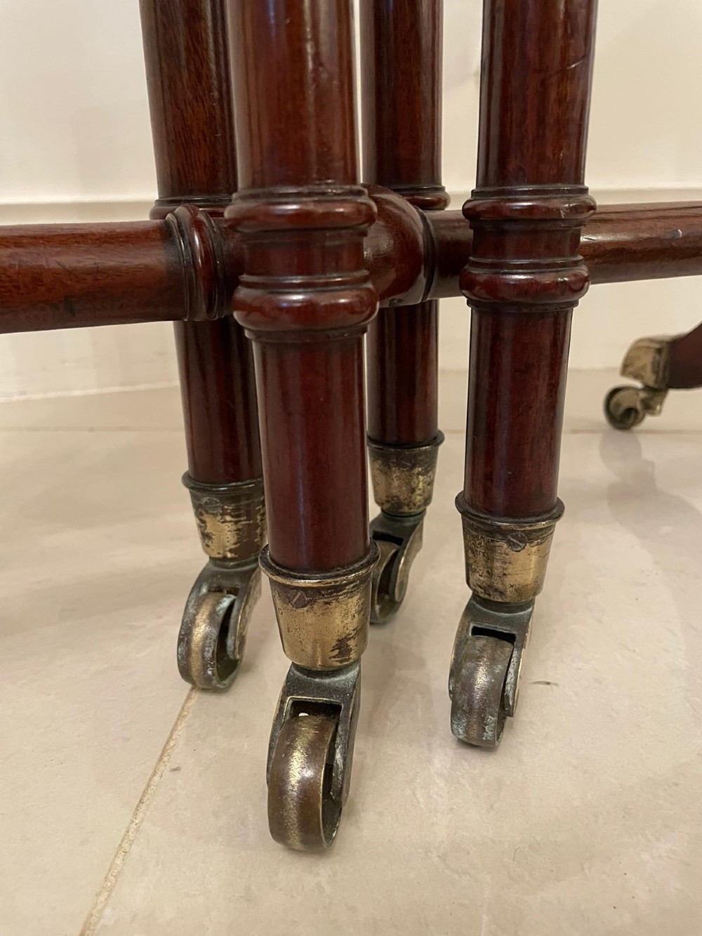 A closed George III mahogany drop-leaf table with slender turned legs, a stretcher base, and brass castors. View II