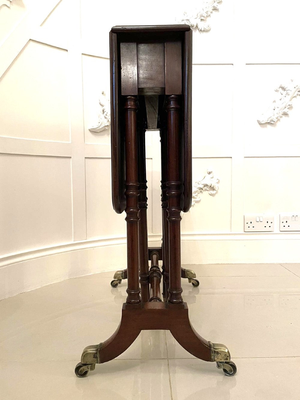 A closed George III mahogany drop-leaf table with slender turned legs, a stretcher base, and brass castors. View III