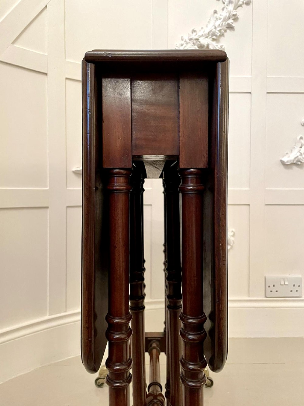 A closed George III mahogany drop-leaf table with slender turned legs, a stretcher base, and brass castors. View IV