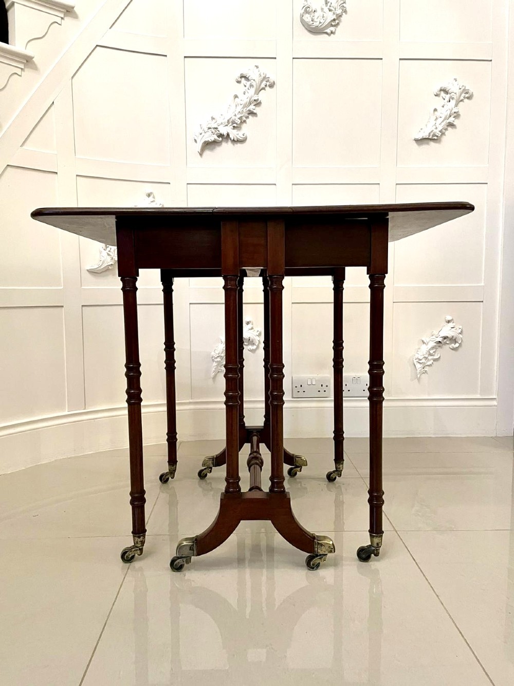A closed George III mahogany drop-leaf table with slender turned legs, a stretcher base, and brass castors. View V