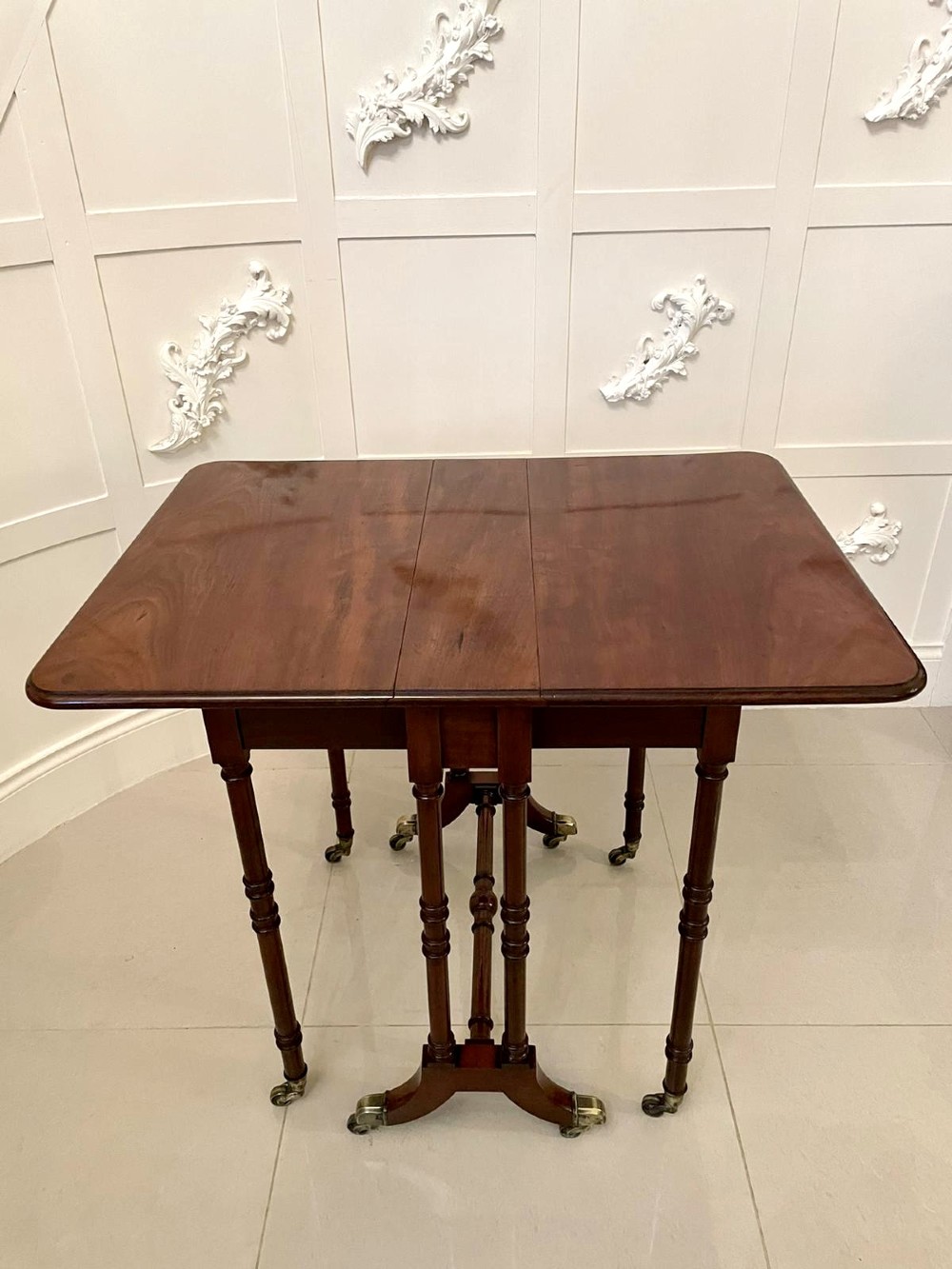 A closed George III mahogany drop-leaf table with slender turned legs, a stretcher base, and brass castors. View VI