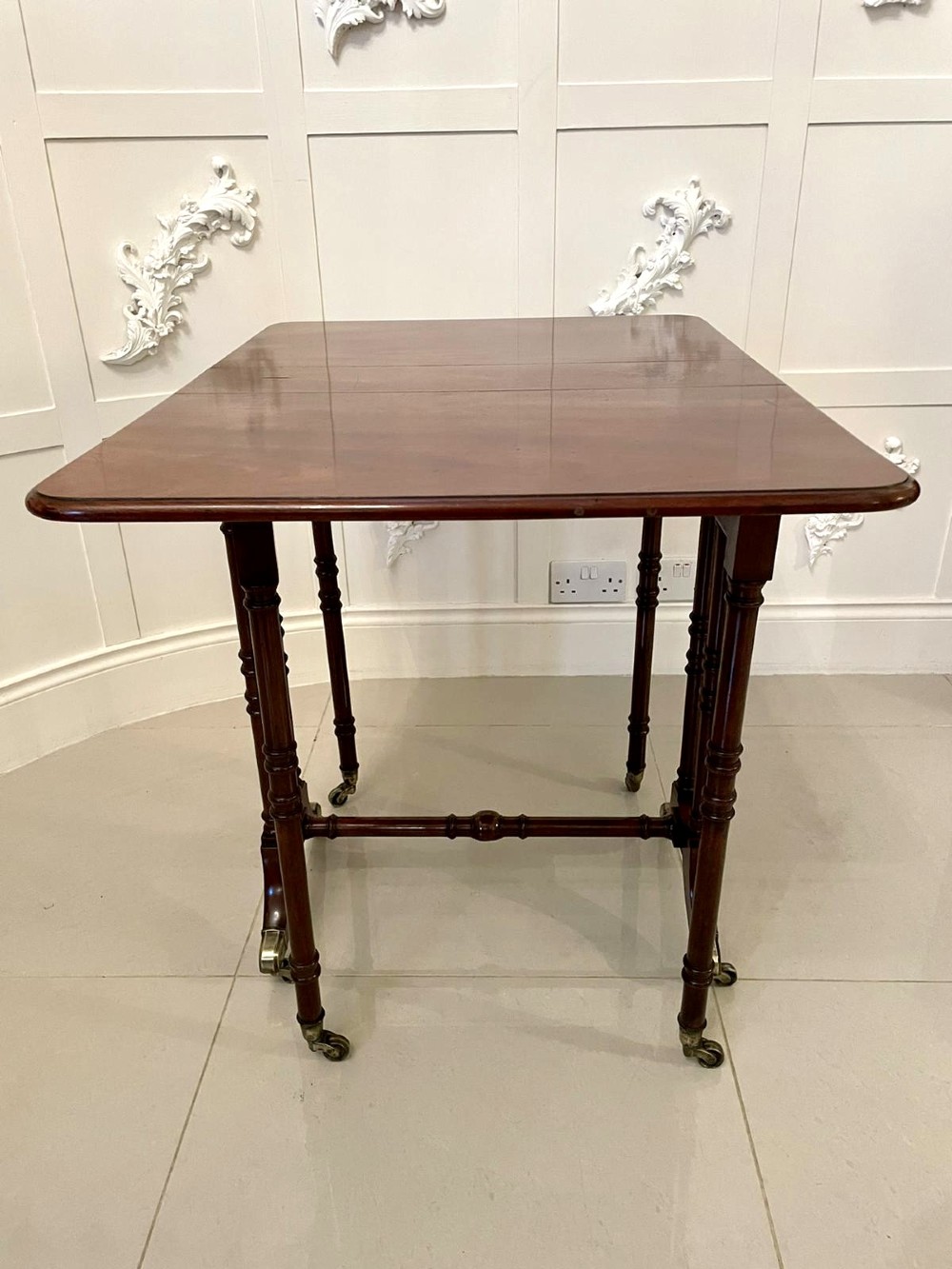 A closed George III mahogany drop-leaf table with slender turned legs, a stretcher base, and brass castors. View VII