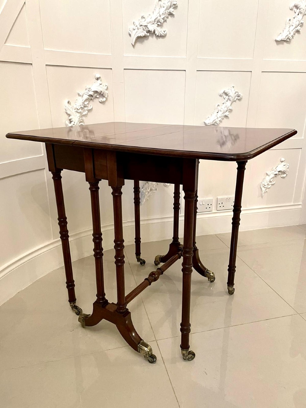 A closed George III mahogany drop-leaf table with slender turned legs, a stretcher base, and brass castors. View VIII