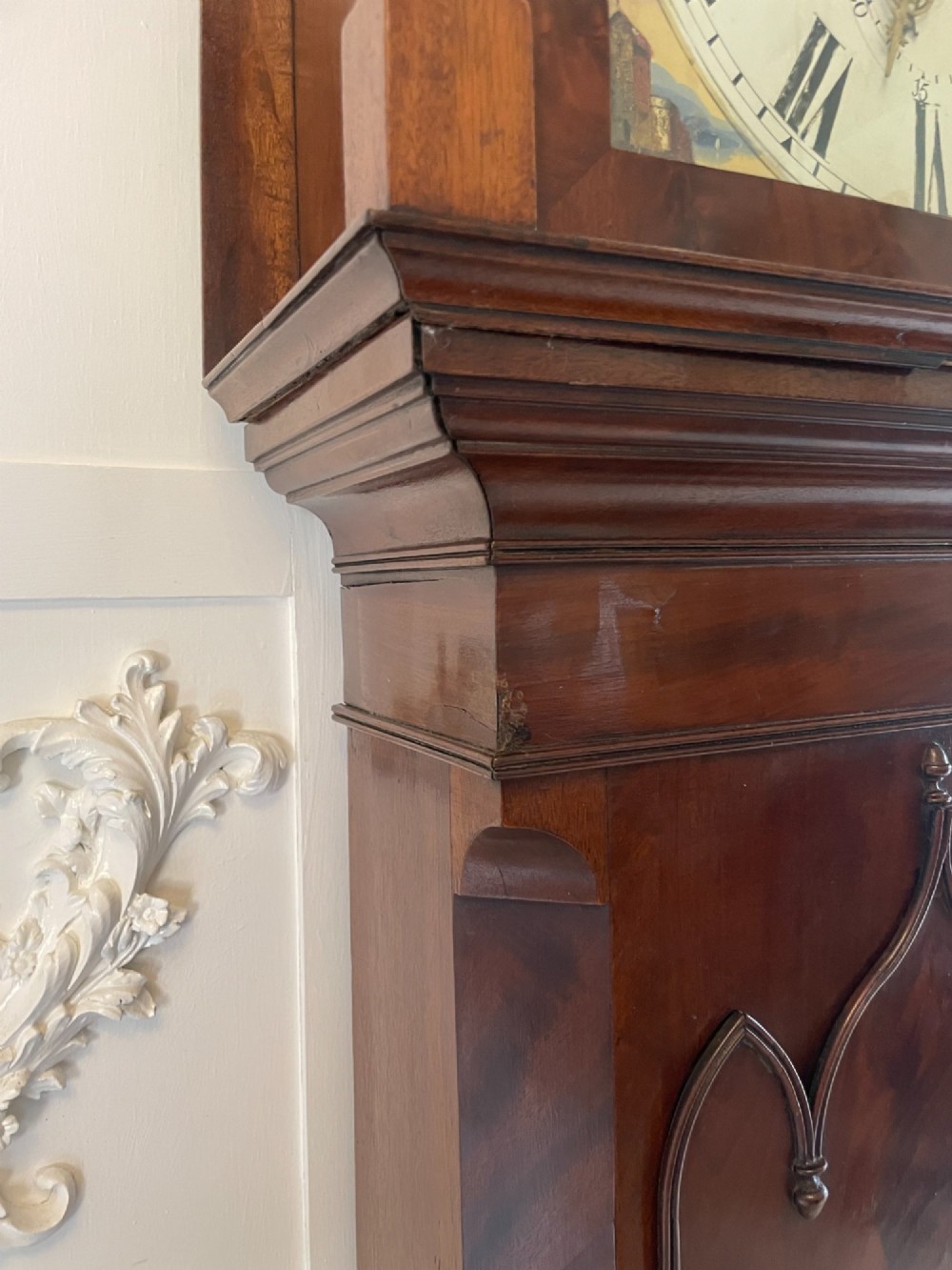 A George III flame mahogany longcase clock featuring a swan-neck pediment, turned hood columns, a painted arch dial, and a gothic-arched trunk door. View II