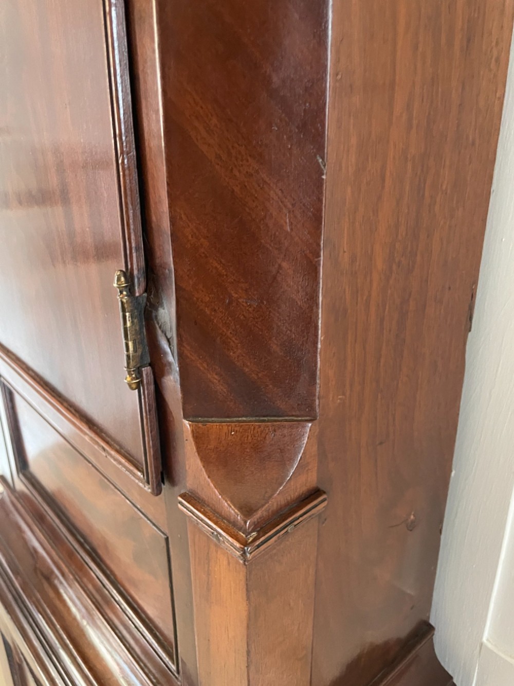 A George III flame mahogany longcase clock featuring a swan-neck pediment, turned hood columns, a painted arch dial, and a gothic-arched trunk door. View III