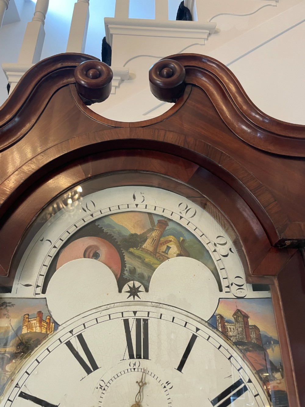 A George III flame mahogany longcase clock featuring a swan-neck pediment, turned hood columns, a painted arch dial, and a gothic-arched trunk door. View VII